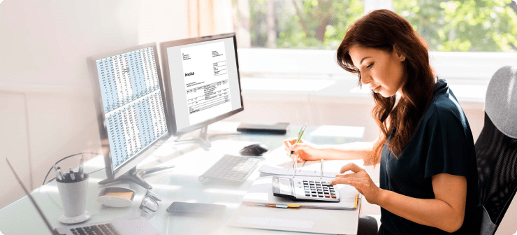 Mujer haciendo cáculos en su calculadora frente a su computador con hojas de Excel en referencia al cálculo de la tasa de retención de los clientes