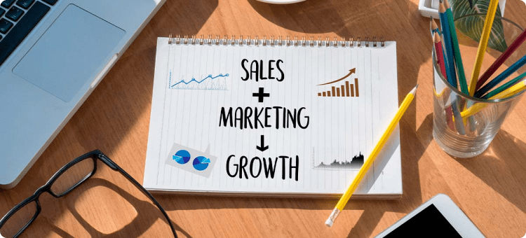 Cuaderno con las palabras ventas + marketing igual a crecimiento en referencia a las estrategias de marketing para aumentar las ventas